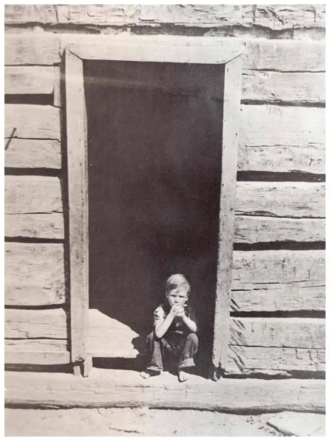  A boy sitting in the doorway of a log cabin